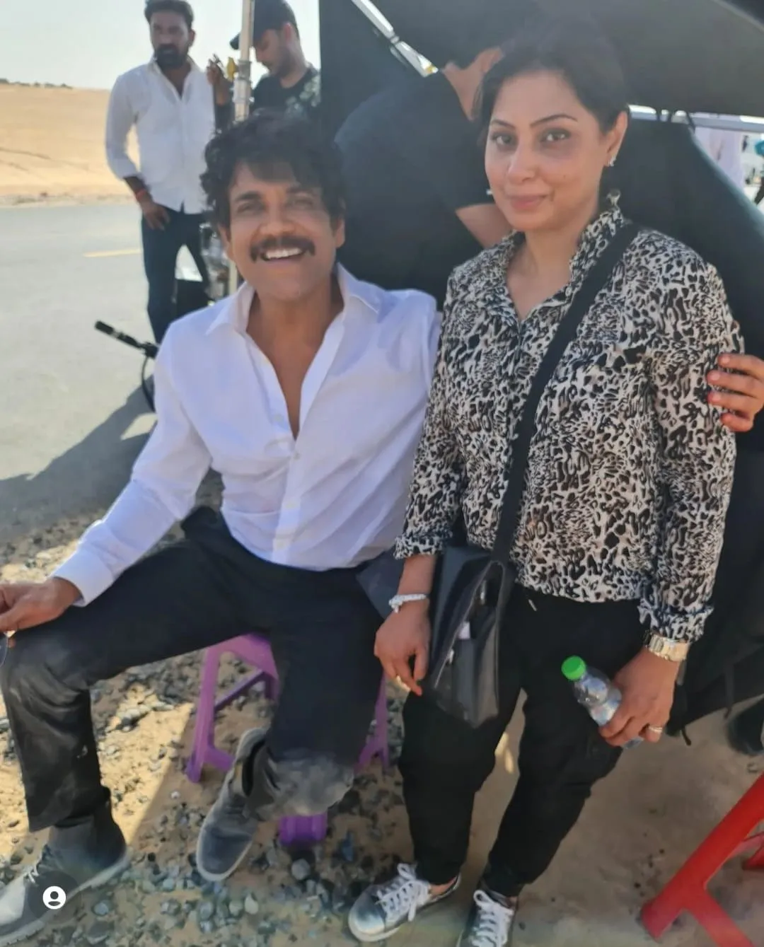 Man in a white shirt seated next to a woman in an animal-print top outdoors