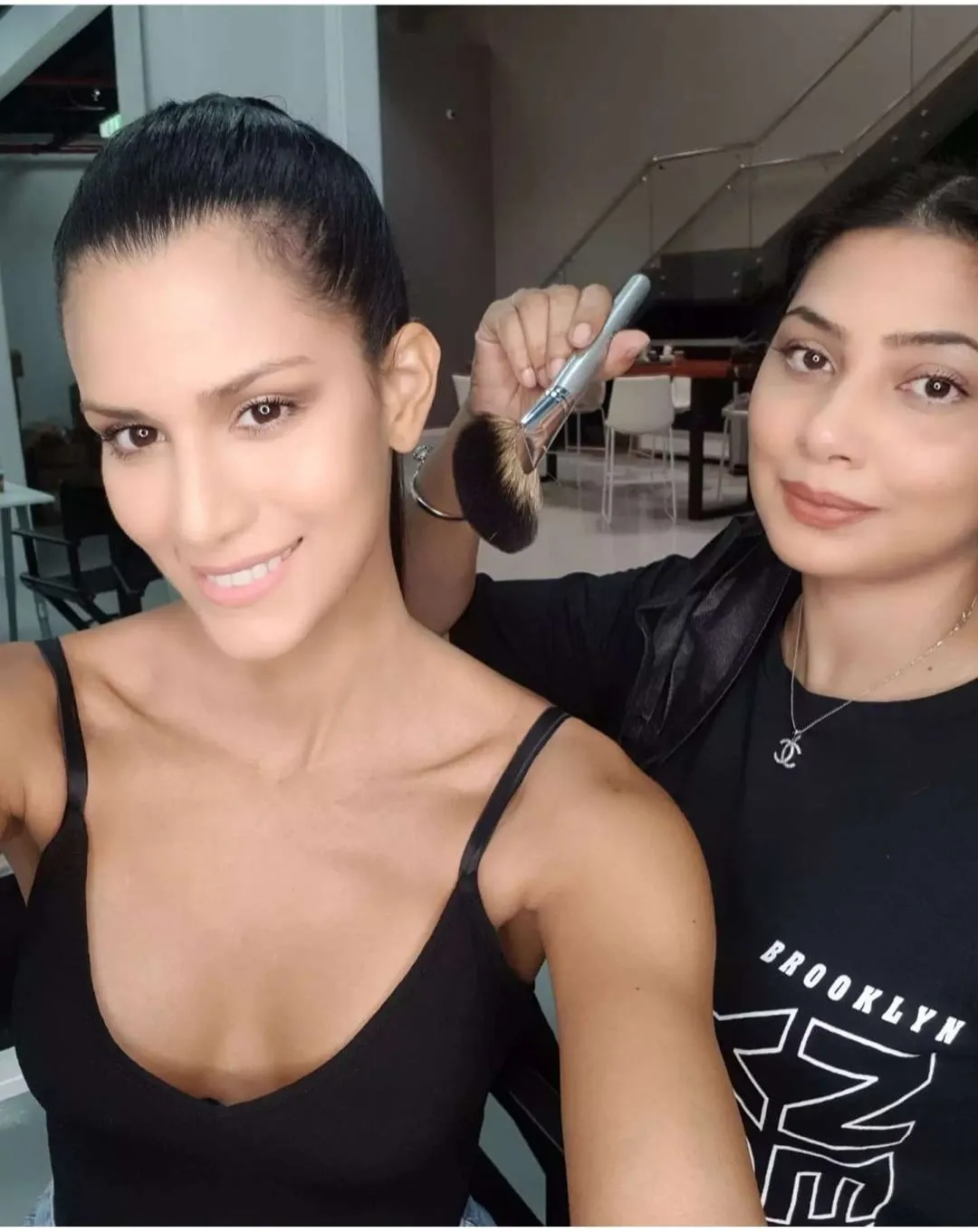 Two women taking a selfie in a bright room, one with long hair in a black tank top