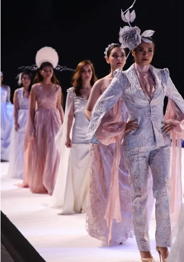 Models in pastel and silver outfits walking down a fashion show runway