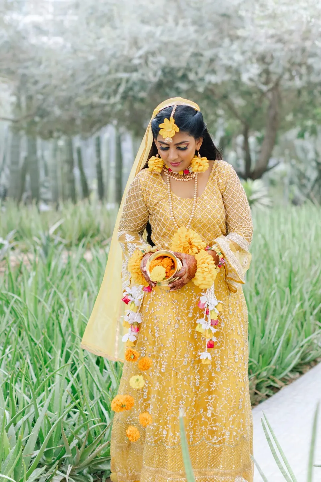 Woman in a yellow outfit with fresh flower jewellery holding a bouquet in a green garden