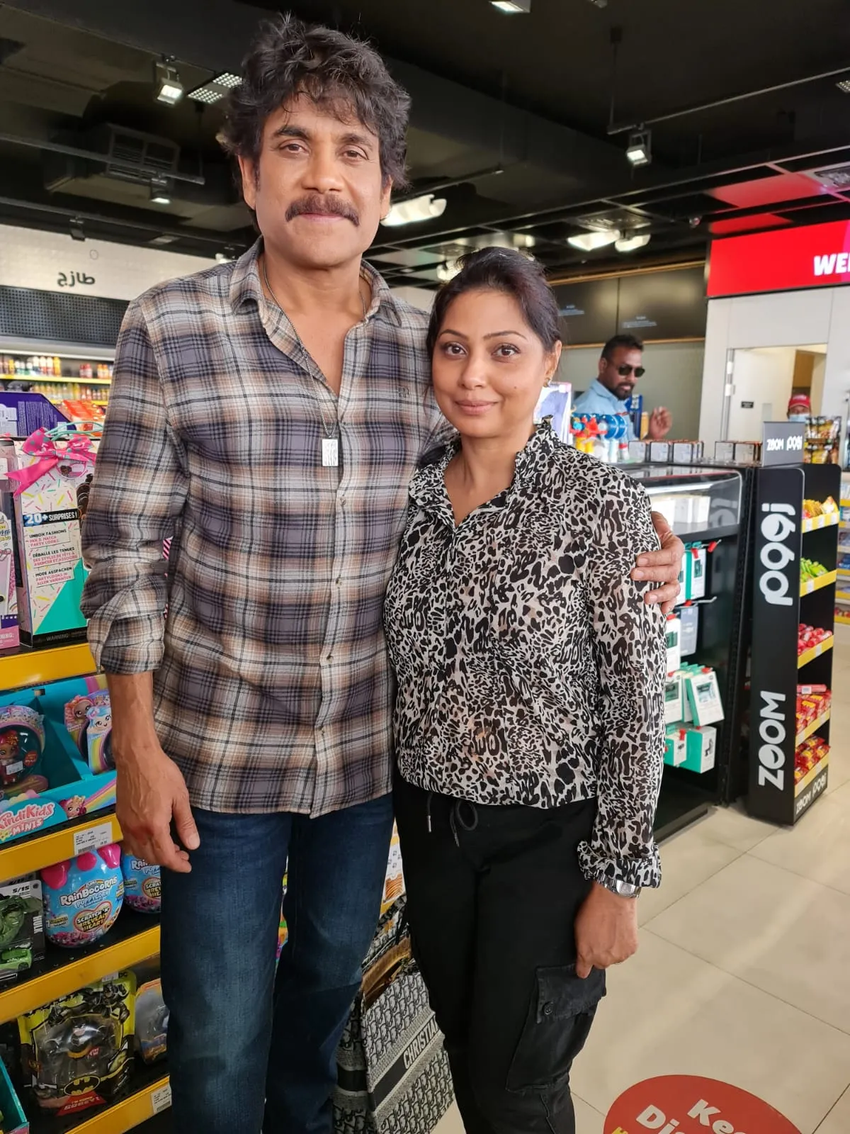 Man in a plaid shirt and woman in an animal-print top posing side by side in a shop aisle, full length
