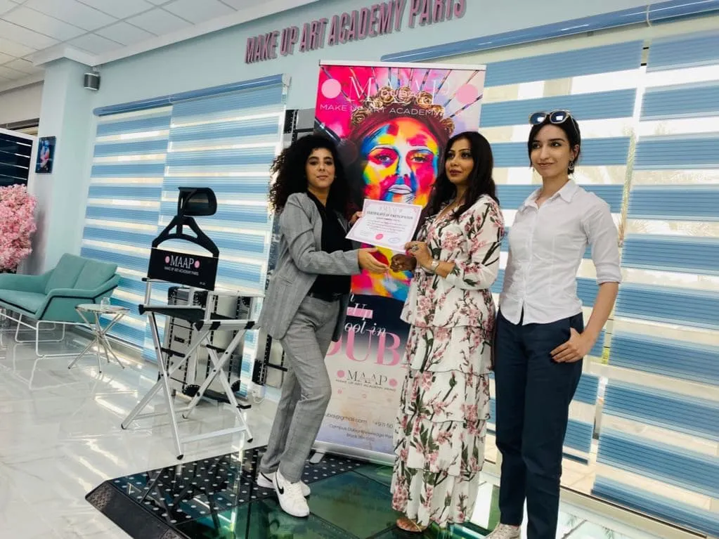 Two women standing in front of a colourful banner in a room with striped blinds