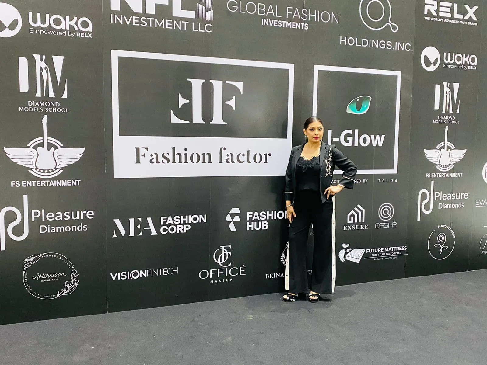 Woman in black standing in front of a fashion event sponsor wall