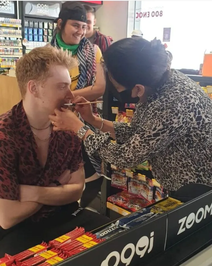 Makeup artist applying makeup to a seated man at a beauty counter with product displays