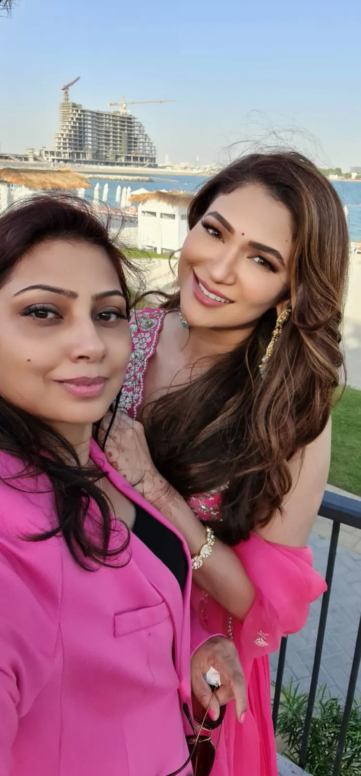 Two women in pink outfits posing together beside the water
