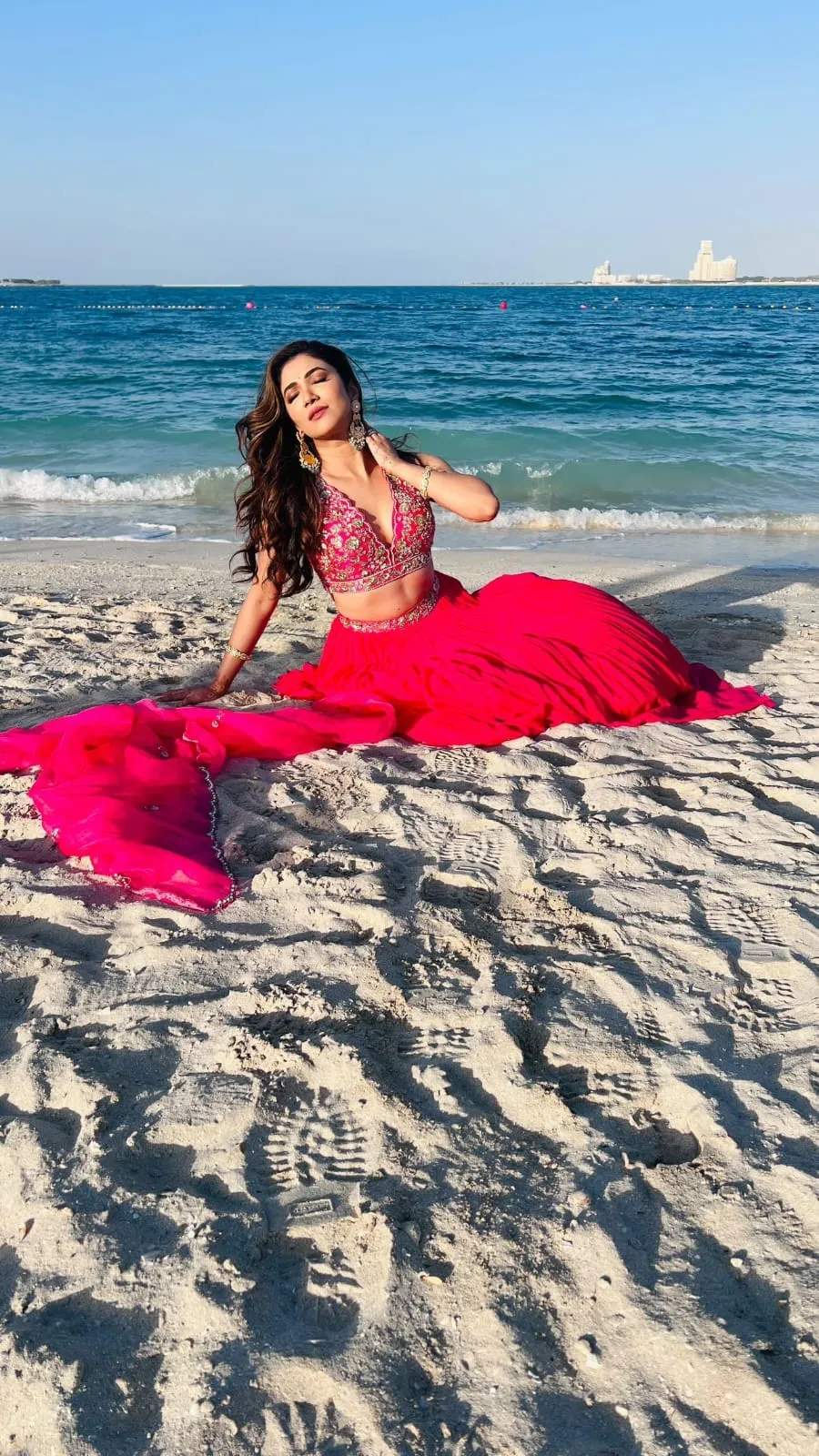 Woman in a magenta skirt sitting on a beach with the sea behind her
