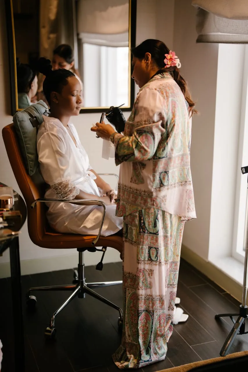Woman seated in an orange armchair in a room while another woman styles her hair