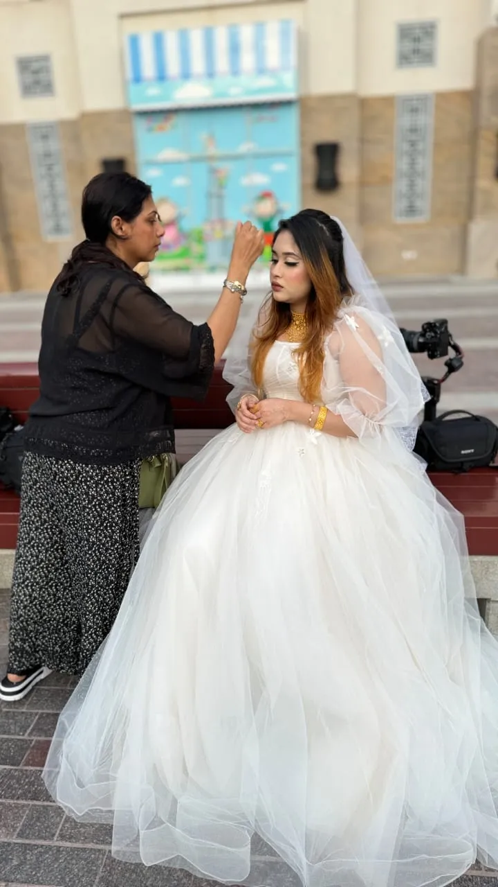 Bride in a white tulle gown outdoors while a makeup artist touches up her face