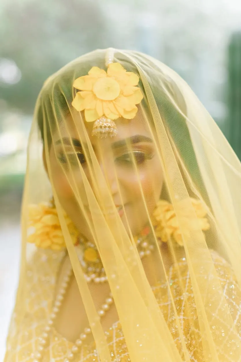 Bride with her face covered by a sheer yellow veil and a yellow flower on her head