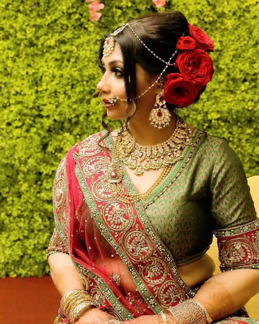 Woman in a green and pink embroidered outfit with red roses in her updo and gold jewellery