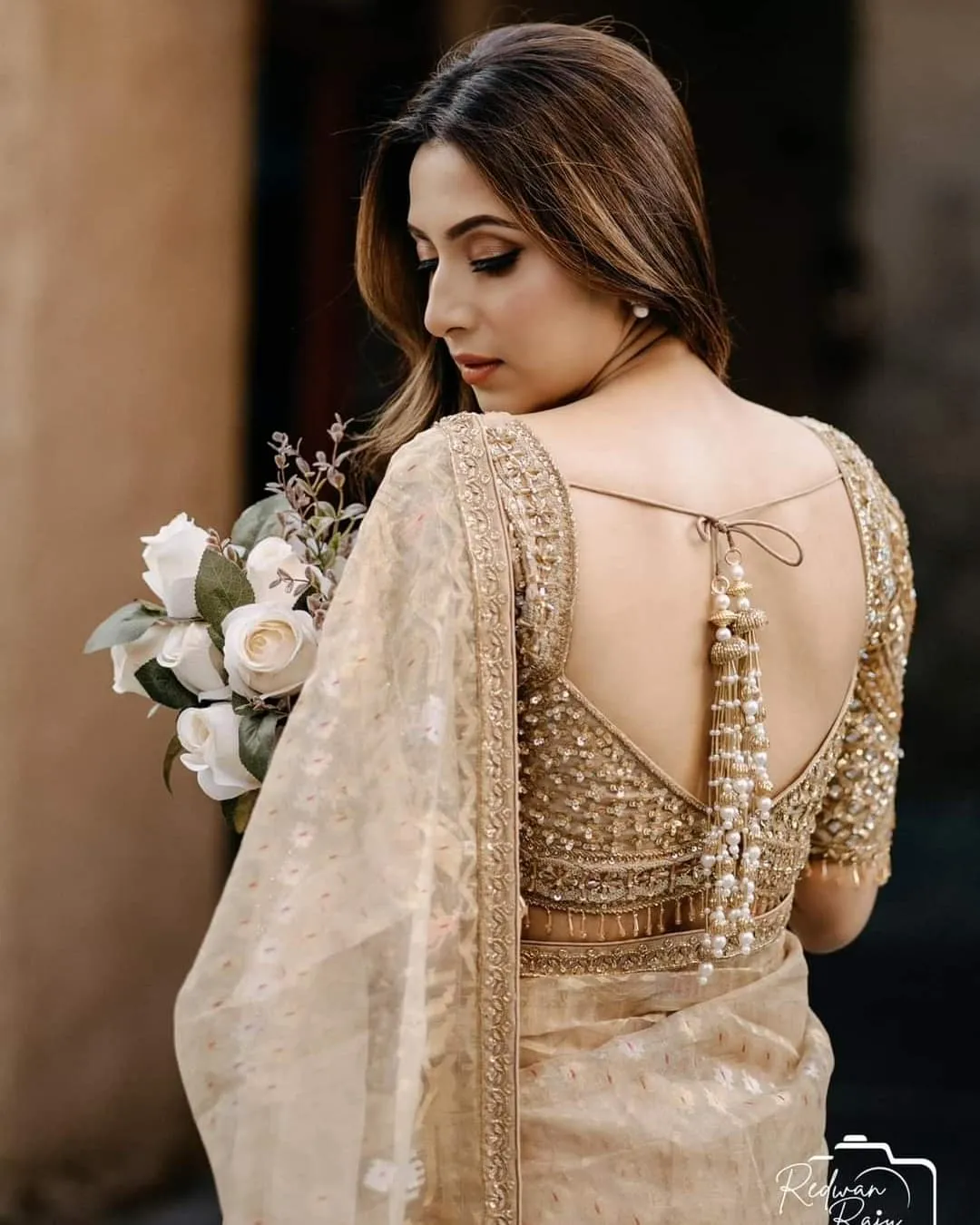 Woman seen from behind in a cream embroidered outfit and veil, holding a white bouquet