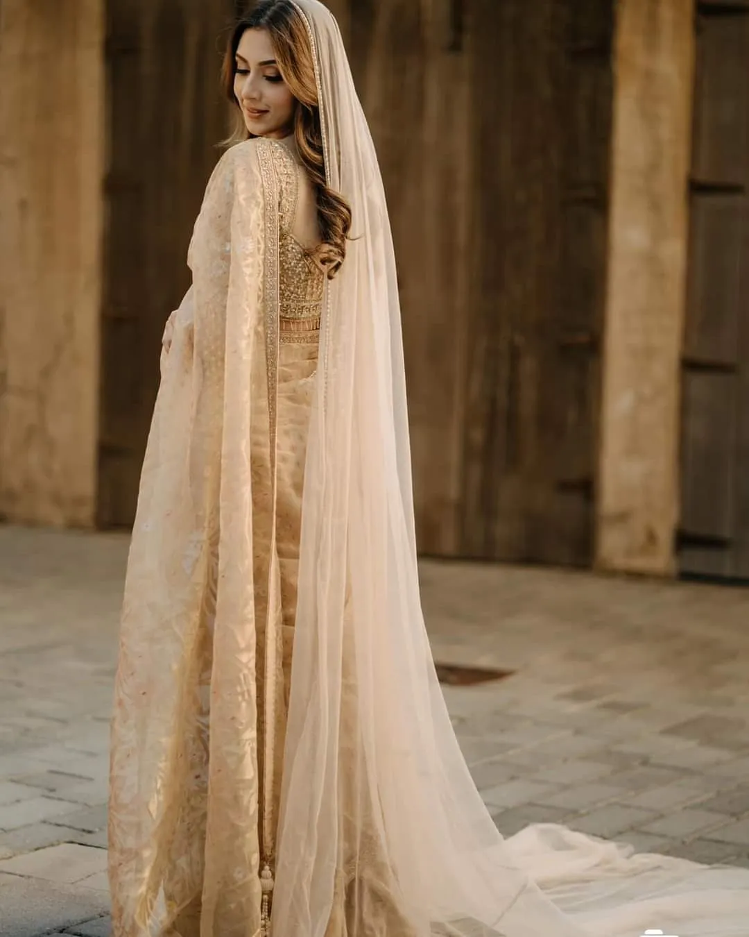 Bride in a cream gown with a long train and sheer veil in front of a wooden door, looking back