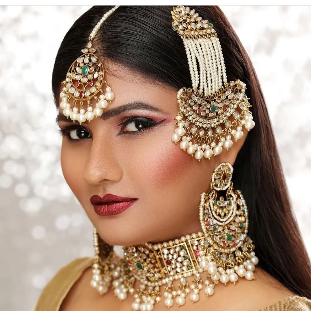 Close-up of a woman wearing a pearl headpiece, nose chain, heavy gold choker and statement earrings