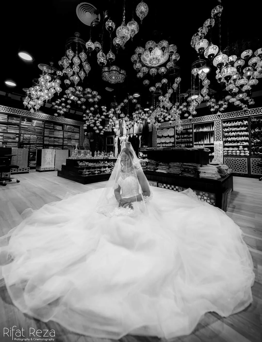 Black and white photo of a bride in a very large white tulle gown in a shop with a floral ceiling