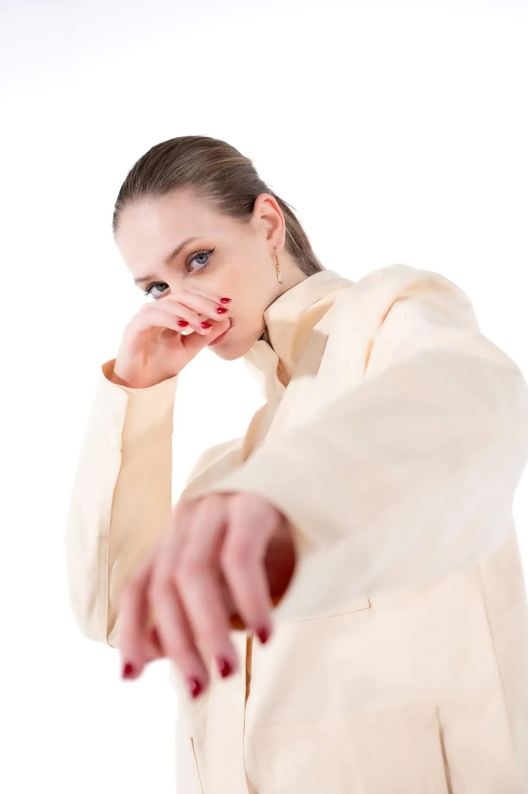 Woman in a cream jacket and red nails reaching towards the camera against a white background