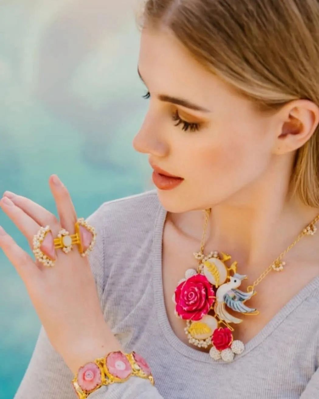 Woman with blonde hair wearing a bold floral statement necklace and colourful rings