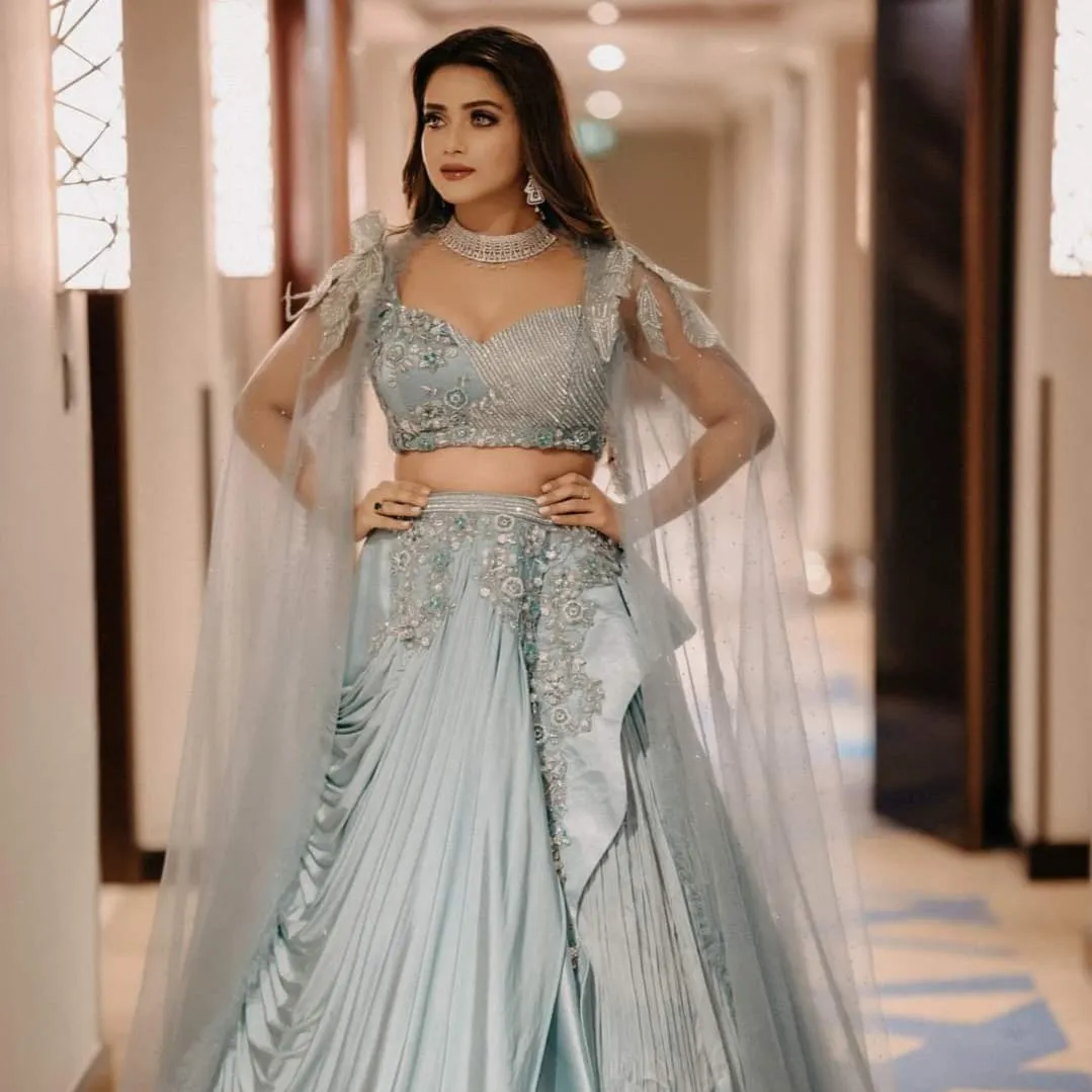 Woman in an embellished sage-green gown with her hands on her hips in a hotel corridor
