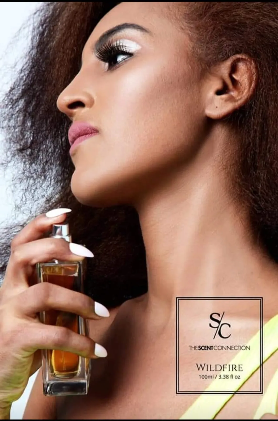 Close-up side profile of a woman holding a perfume bottle, with long nails