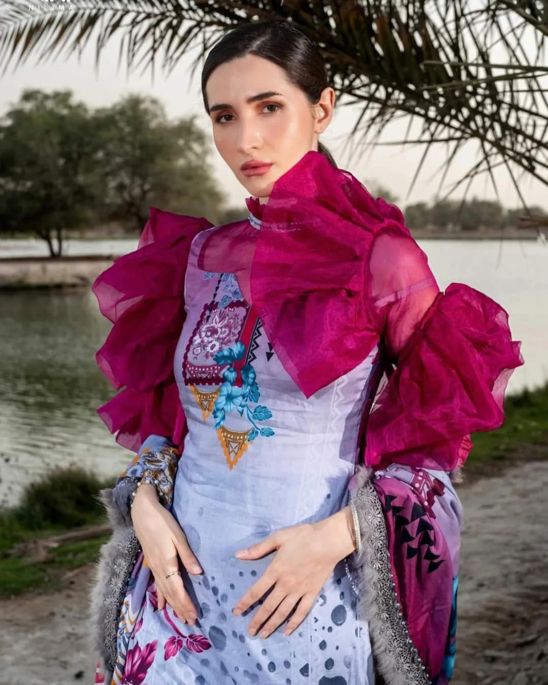 Woman in a colourful floral gown with pink ruffled sleeves standing beside a creek