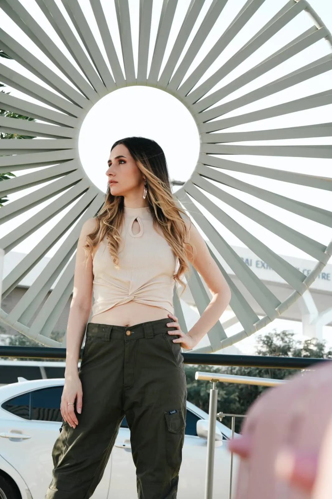 Woman in a beige top and olive trousers standing in front of a large white circular structure