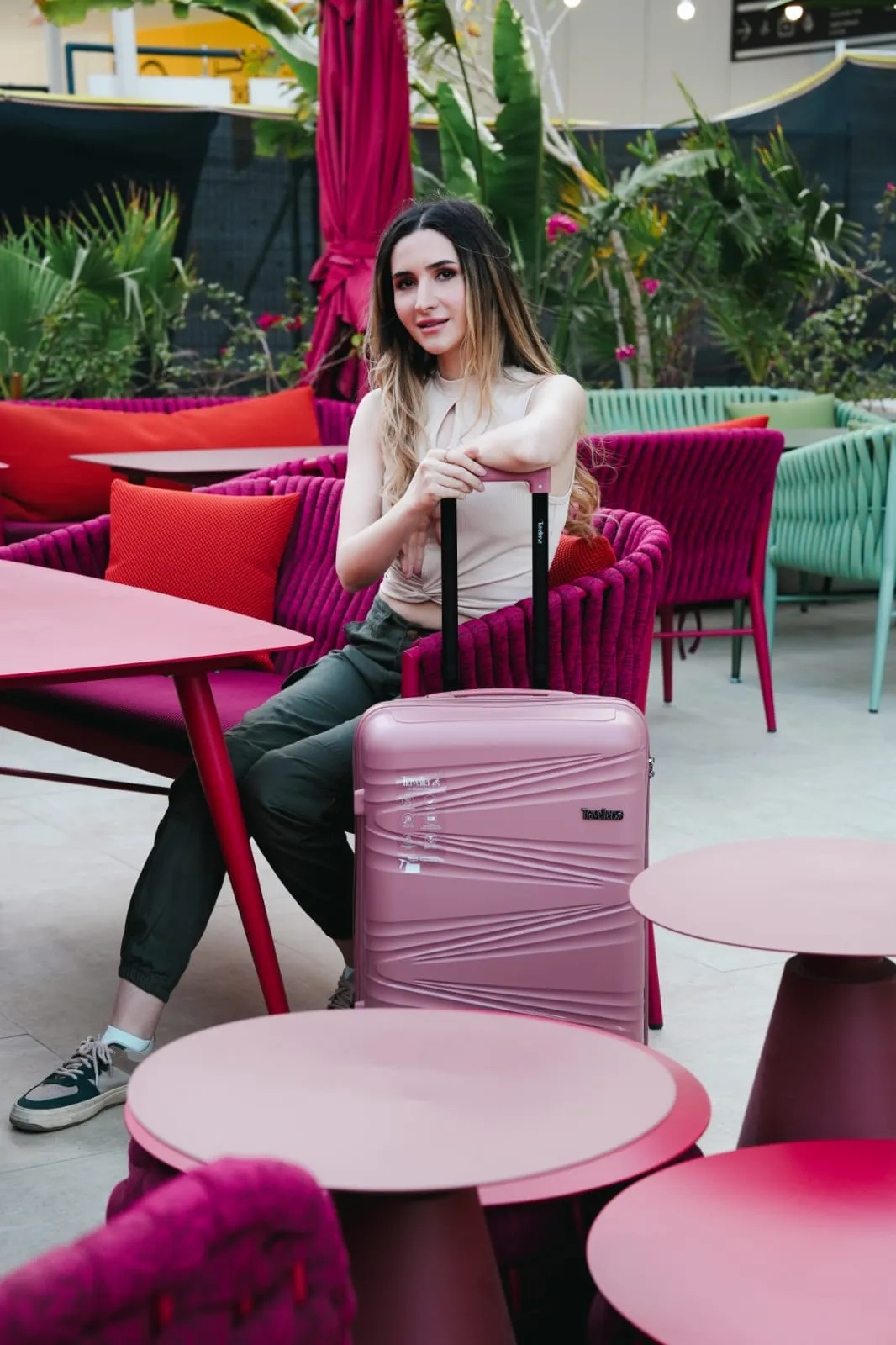 Woman in a white top sitting on a pink lounge with a pink suitcase at a cafe