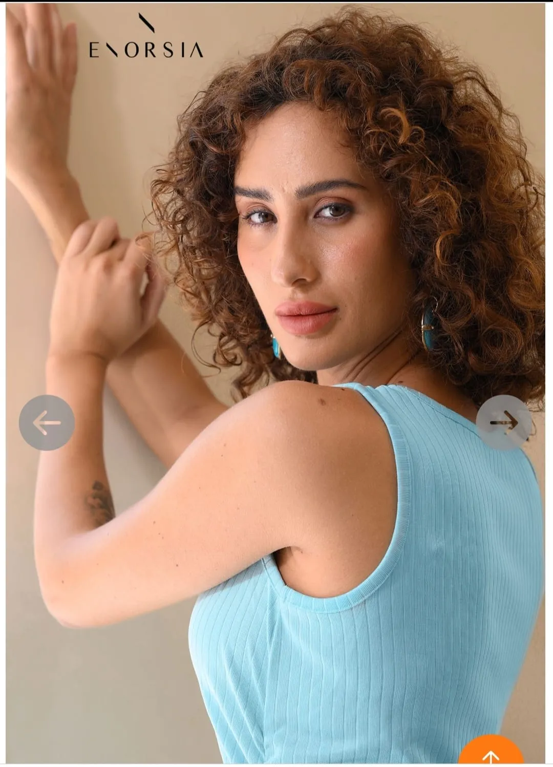 Woman with curly hair in a light-blue sleeveless top with a hand on her shoulder