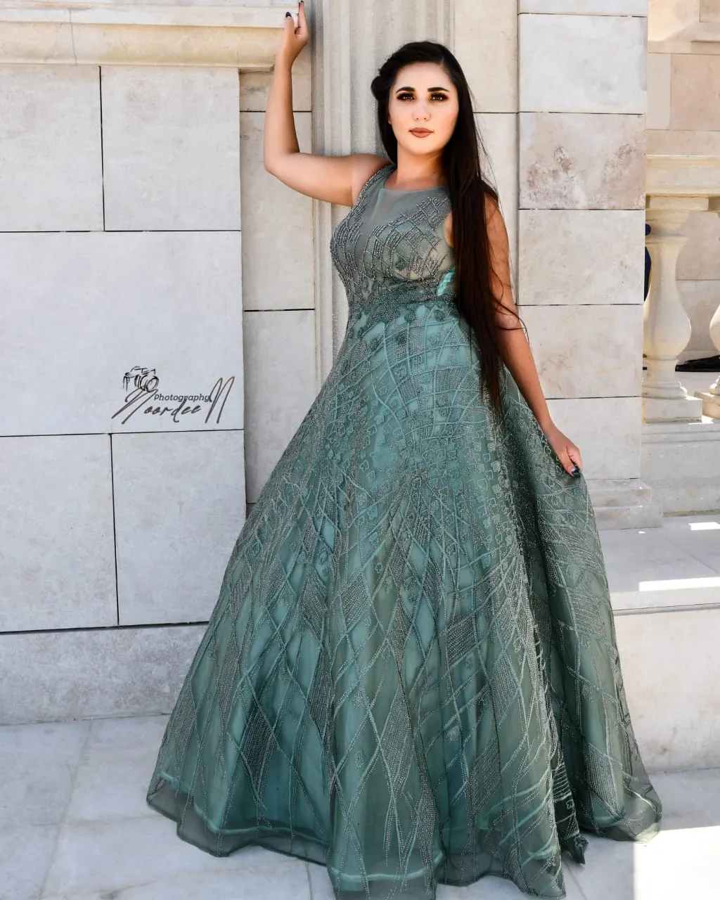 Woman in a long sage-green embellished gown posed against a sandstone wall