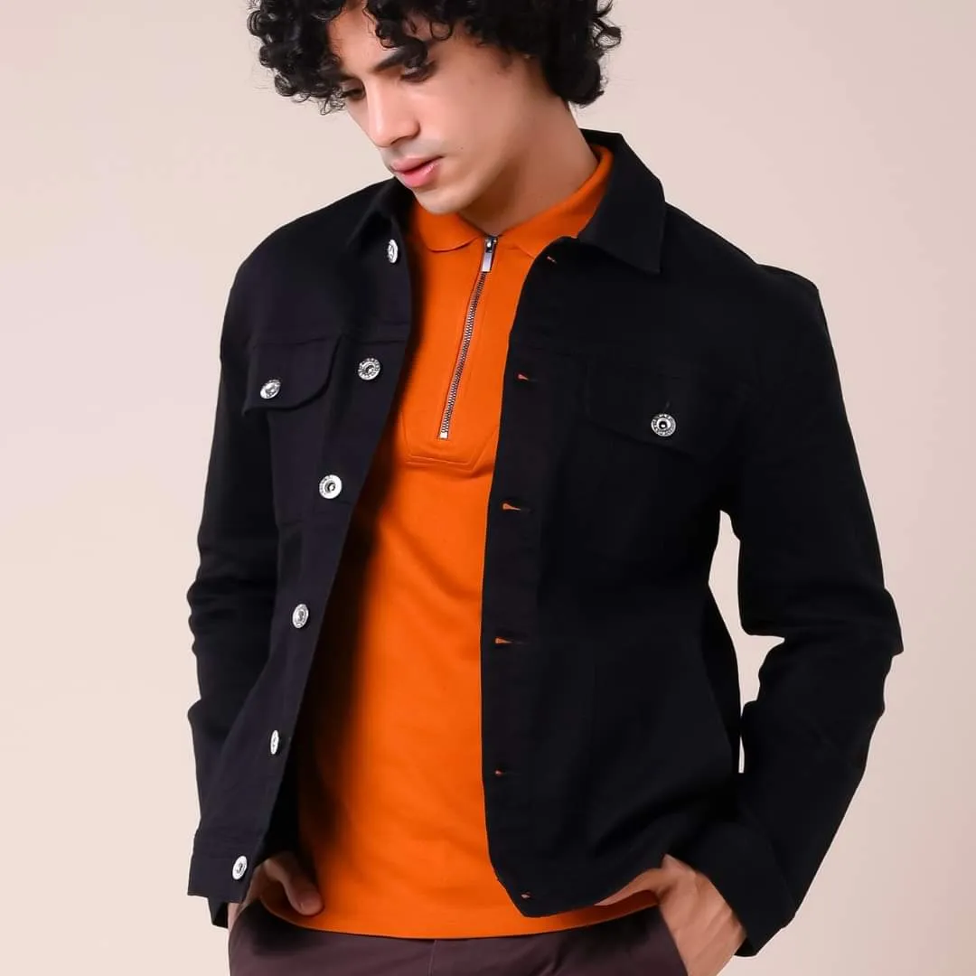 Young man with curly hair in a black denim jacket over an orange top against a beige backdrop