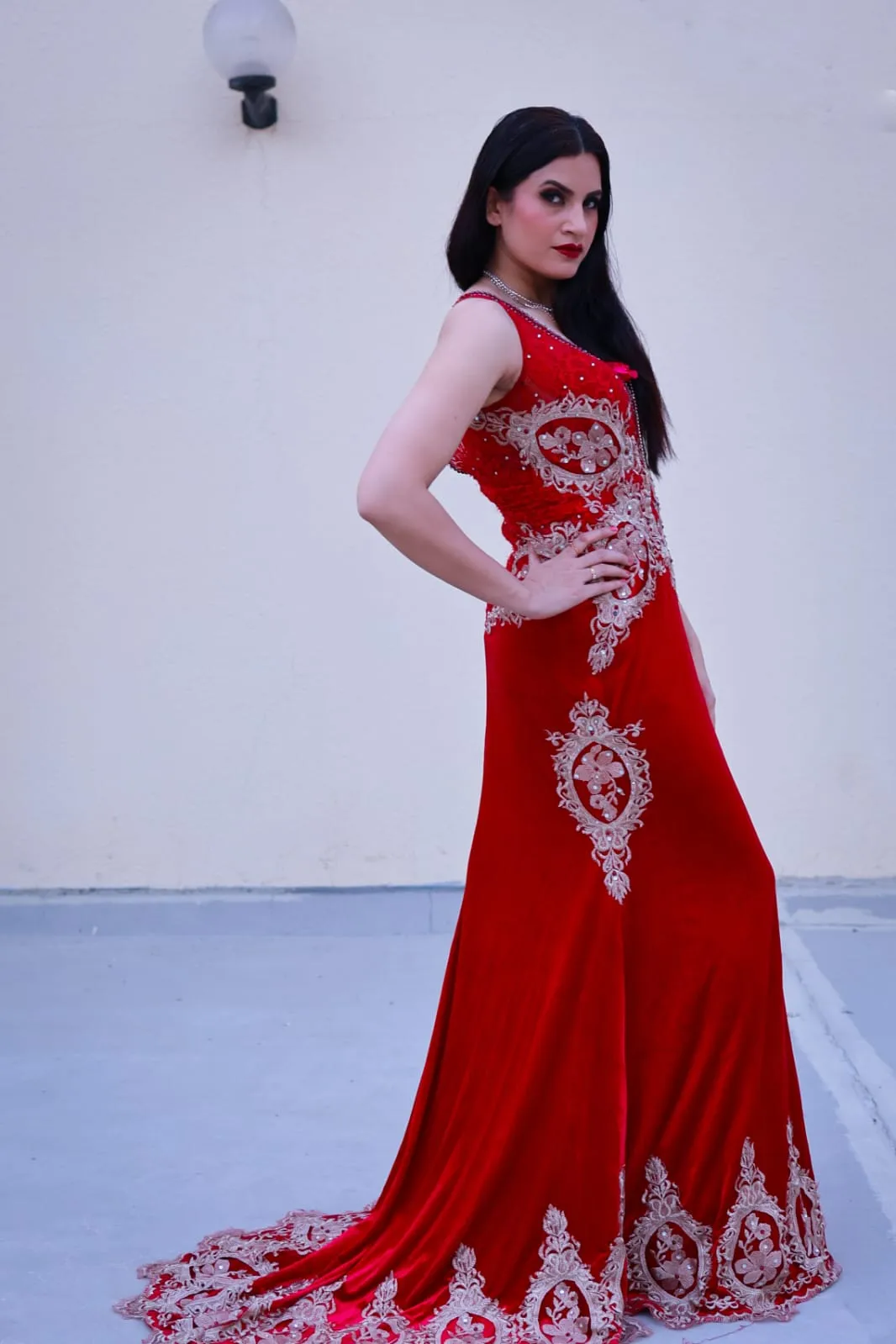Woman in a long fitted red gown with a white embroidered hem standing on a white floor